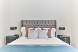 A neatly made bed with a tufted headboard, two bedside tables with lamps, and a blue throw blanket.