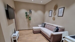 A modern living room with a sectional sofa, a small white table, and a white chair. - PICCOLE DONNE (Naples)