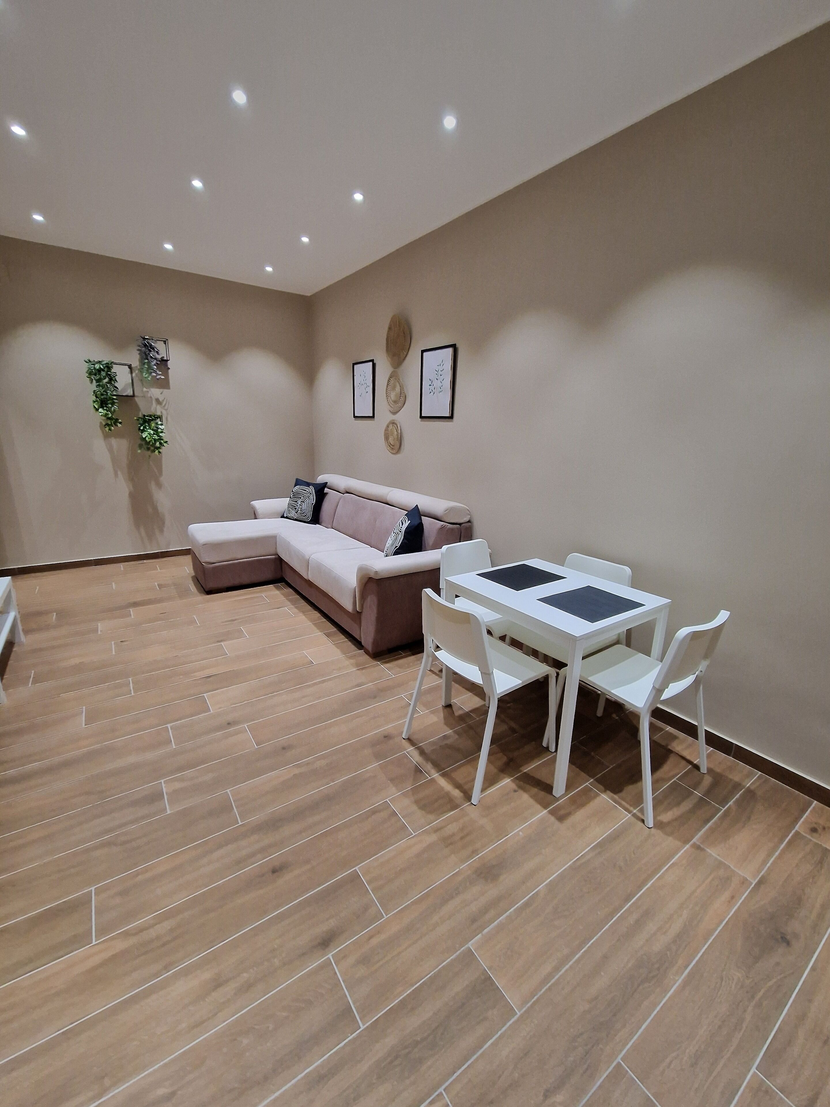 Un moderno salón con un sofá beige, una mesa de comedor blanca con sillas y suelo de madera.