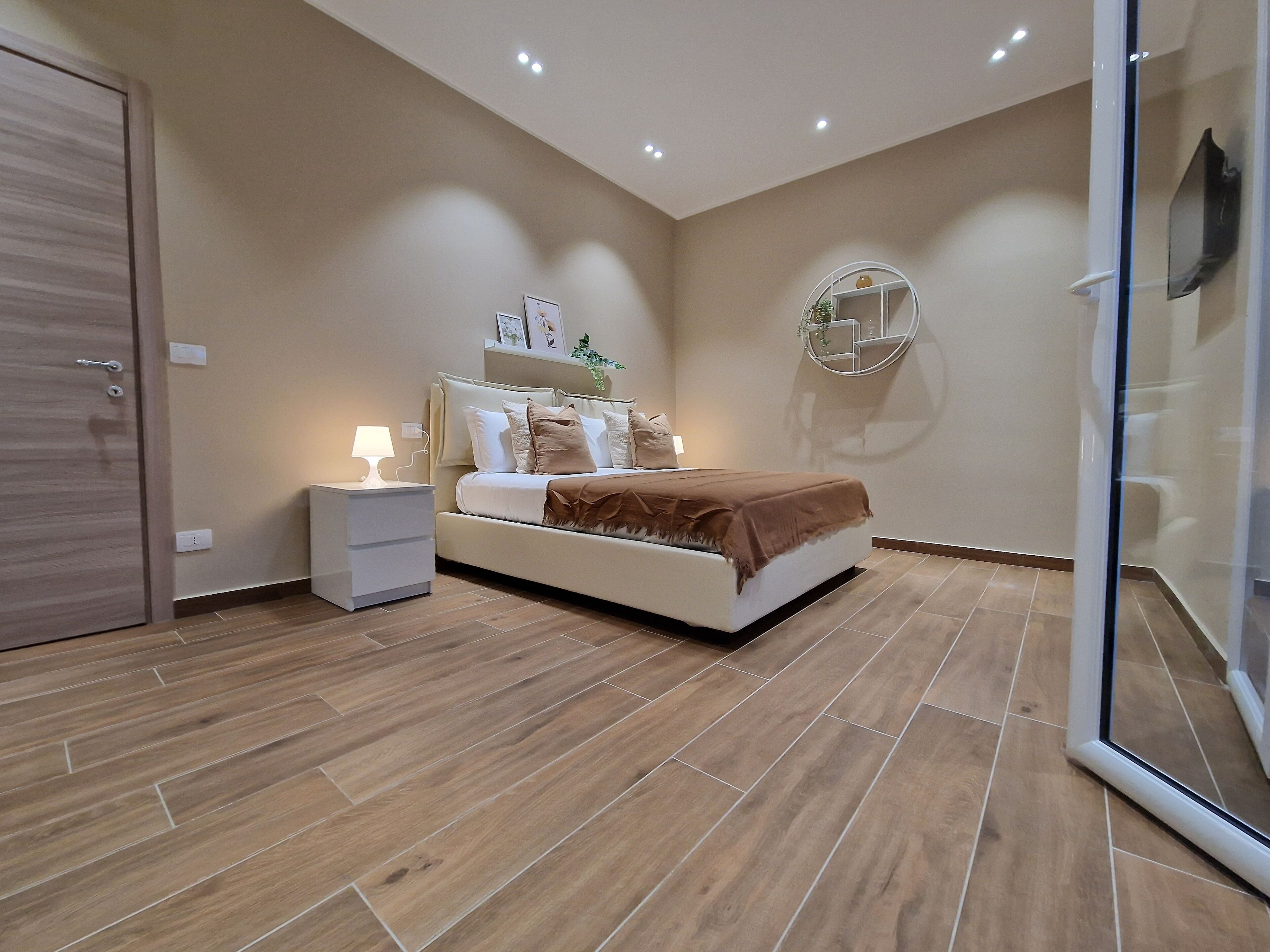 A bedroom with a bed, bedside table, lamp, and a wall-mounted shelf.