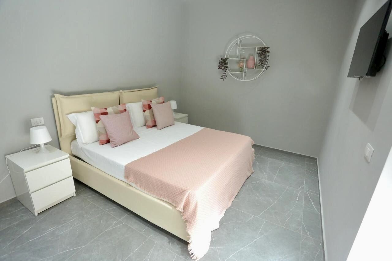A bedroom with a bed, nightstands, a wall-mounted TV, and a decorative mirror.