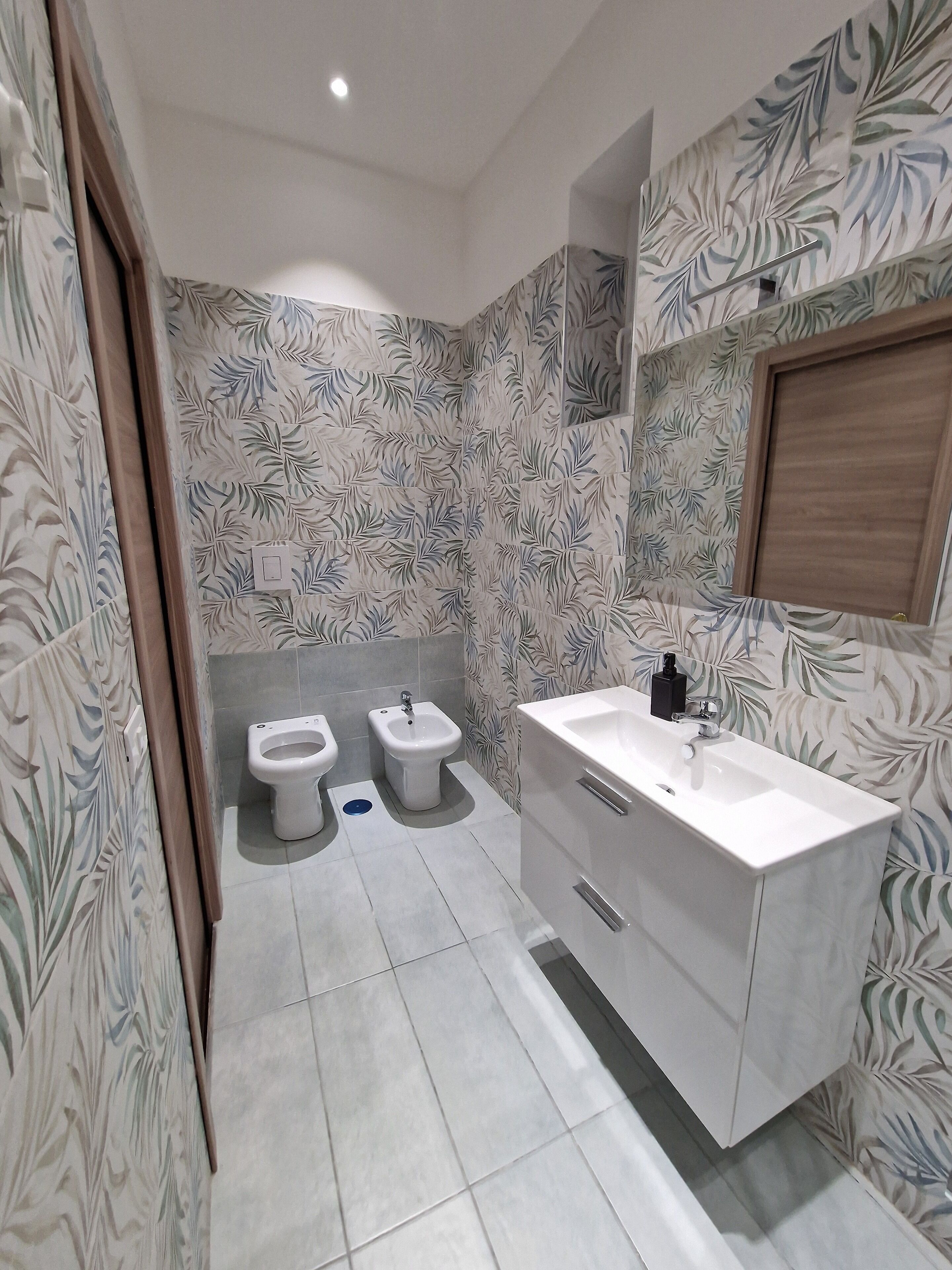 A bathroom with two toilets, a bidet, a sink, and a mirror.
