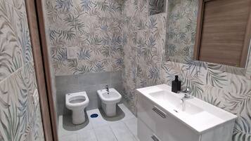 A bathroom with two toilets, a bidet, a sink, and a mirror.