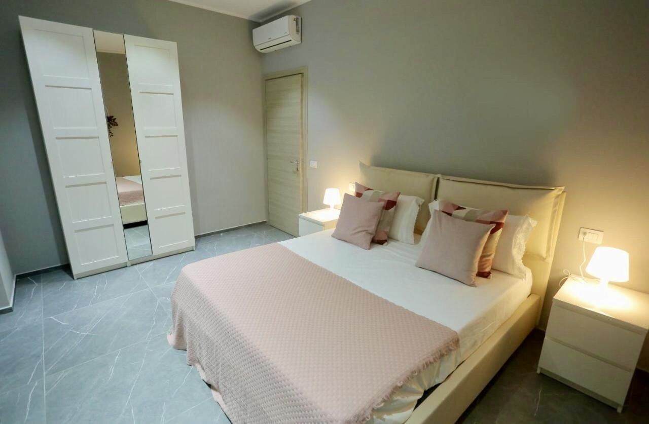 Un dormitorio con cama, lámparas de noche, mesita de noche, armario y aire acondicionado.