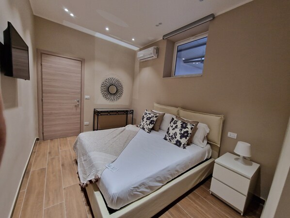 Une chambre à coucher comprenant un lit, une table de chevet, une commode, un climatiseur fixé au mur et un élément décoratif mural.