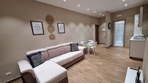 A modern living room with a beige sofa, a dining table, and a kitchen area with a gas stove. - PICCOLE DONNE (Naples)