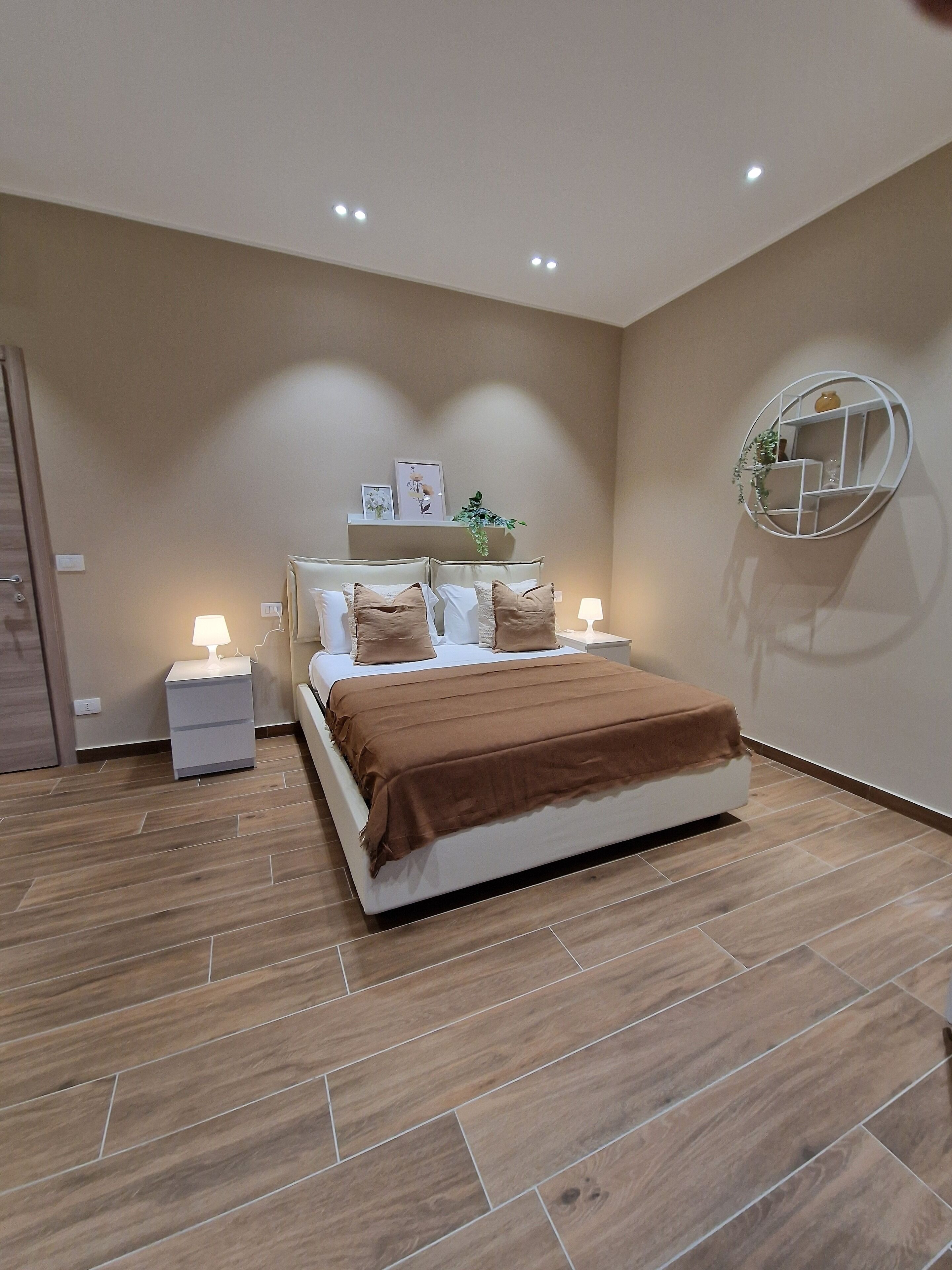Een moderne slaapkamer met een bed, nachtkastjes, een spiegel aan de muur en inbouwspots.