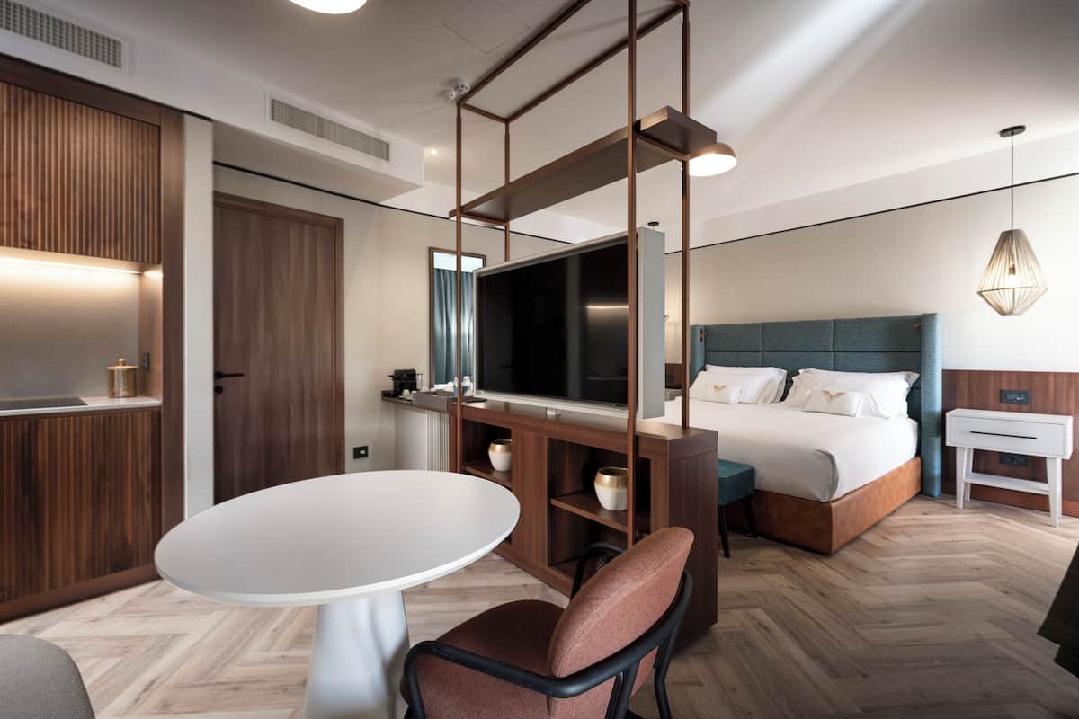 Une chambre d’hôtel moderne avec un lit, une télévision, un lambris en bois, une table de salle à manger ronde et une chaise.