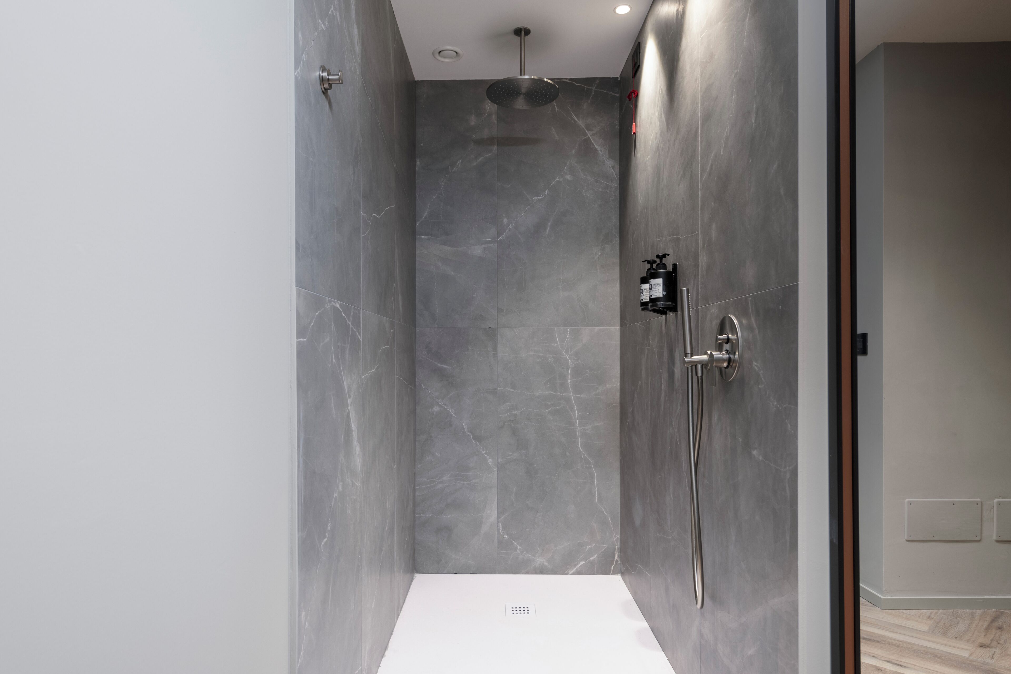 Een moderne douche met een marmeren wand, een handdouche en een muurbevestigde kraan.