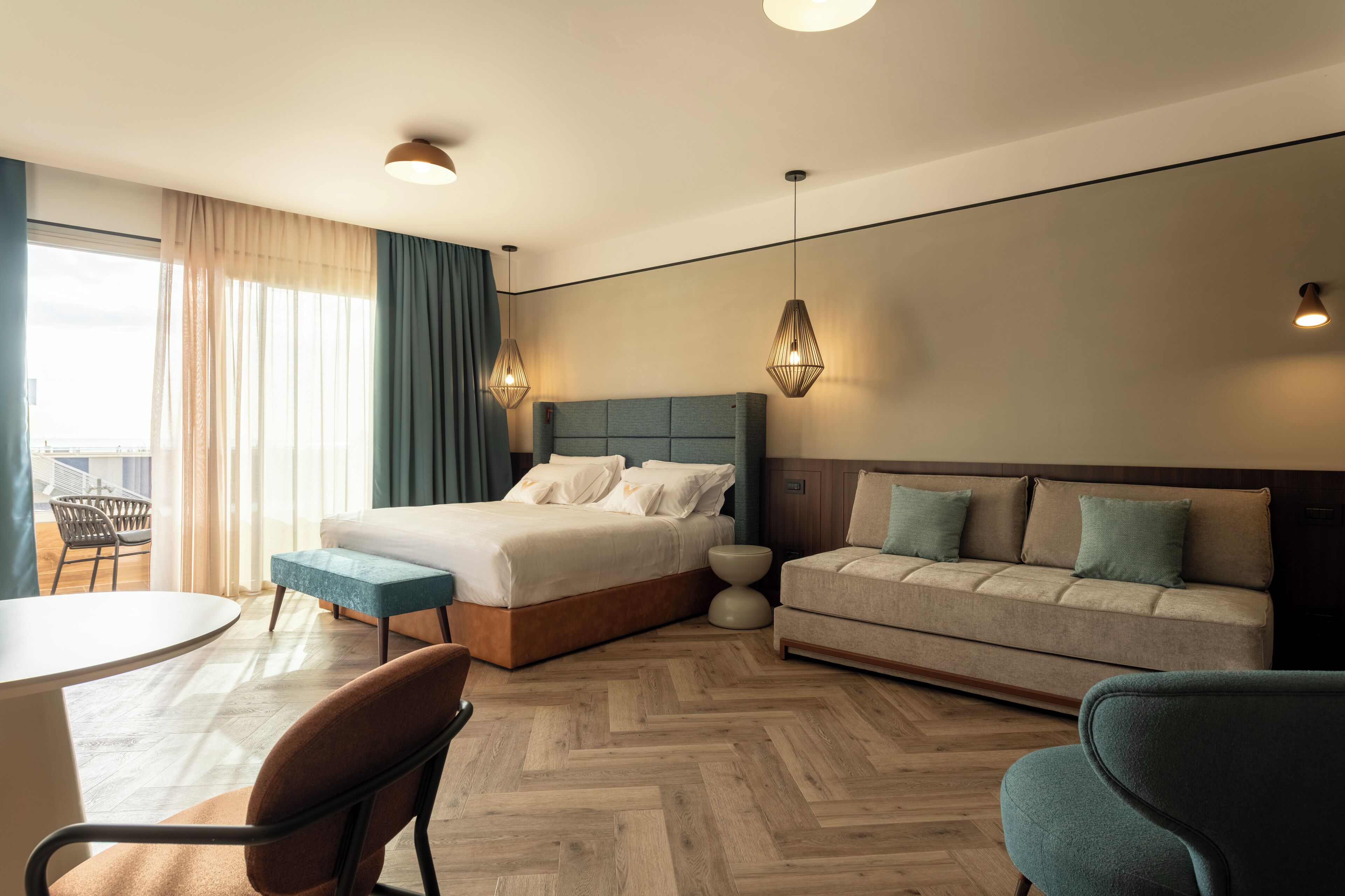 A modern hotel room with a large bed, a sofa, a dining table, and a chair.