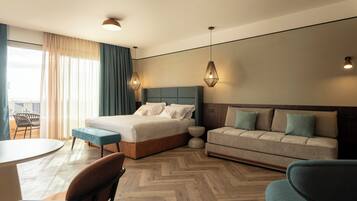 A modern hotel room with a large bed, a sofa, a dining table, and a chair.