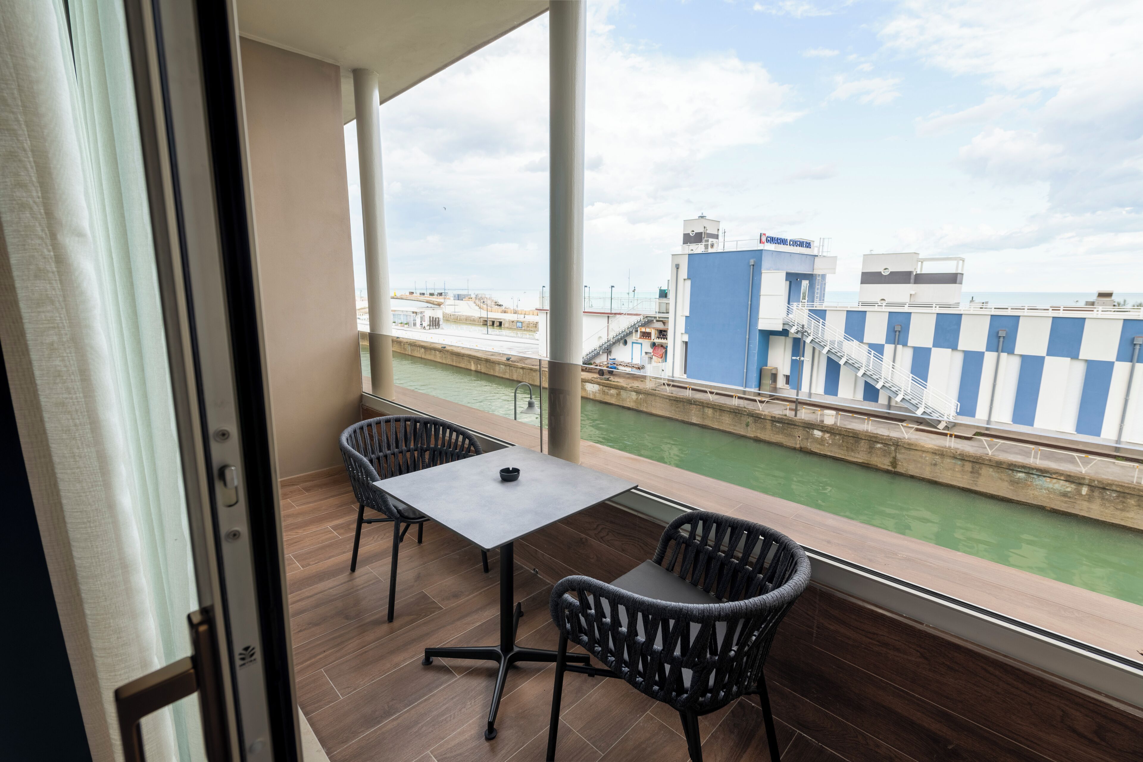 A balcony with a table and chairs, a view of a canal, and a building with a blue and white striped awning.