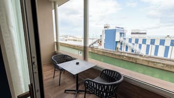 A balcony with a table and chairs, a view of a canal, and a building with a blue and white striped awning.