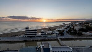 Un pueblo costero con un puerto deportivo, edificios a lo largo del frente marítimo y un atardecer sobre el mar.