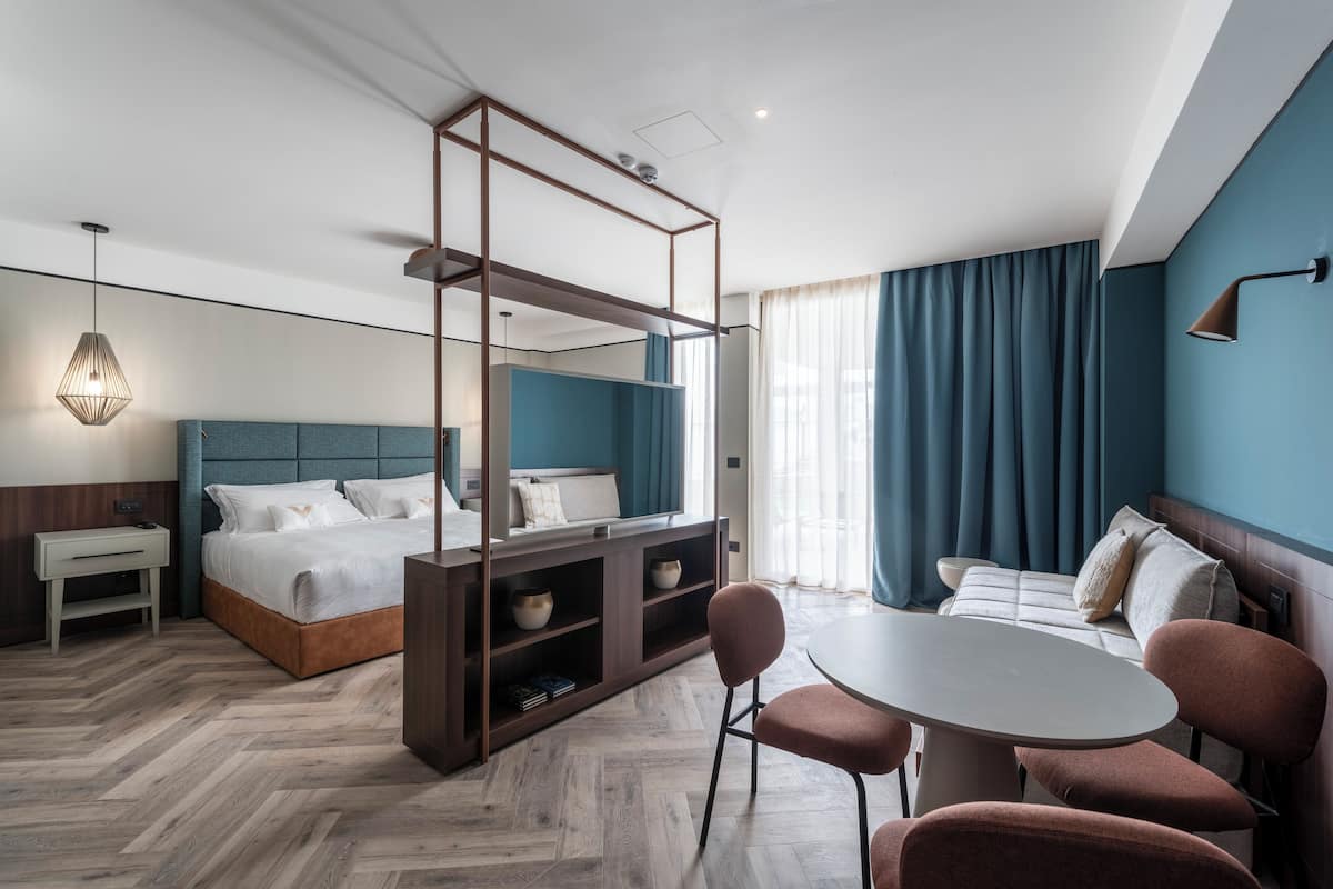 Une chambre d’hôtel moderne équipée d’un lit, d’un bureau, d’une chaise, d’une table et d’une grande fenêtre avec des rideaux.