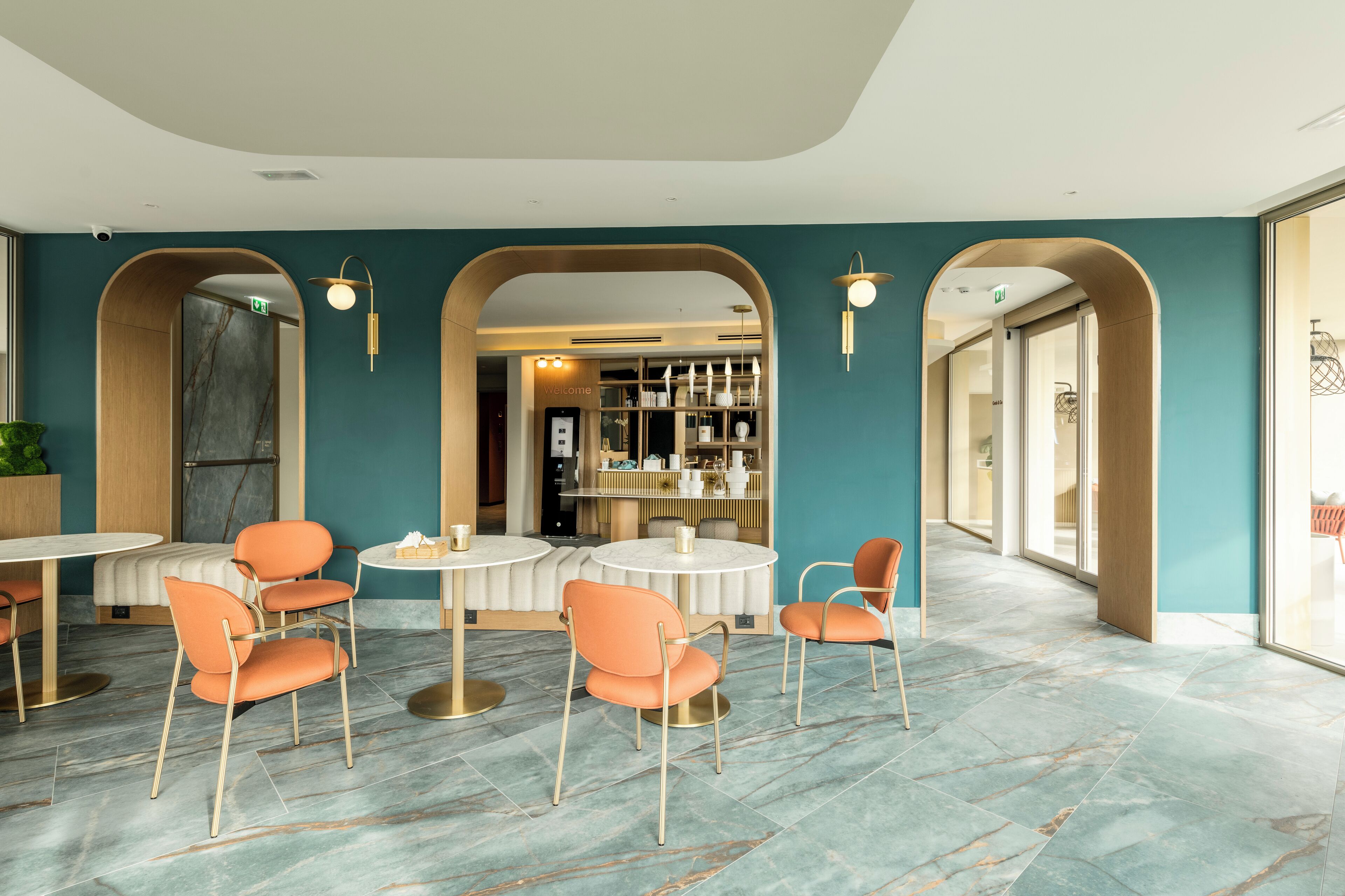 A modern interior with teal walls, marble flooring, and orange chairs around a central round table.