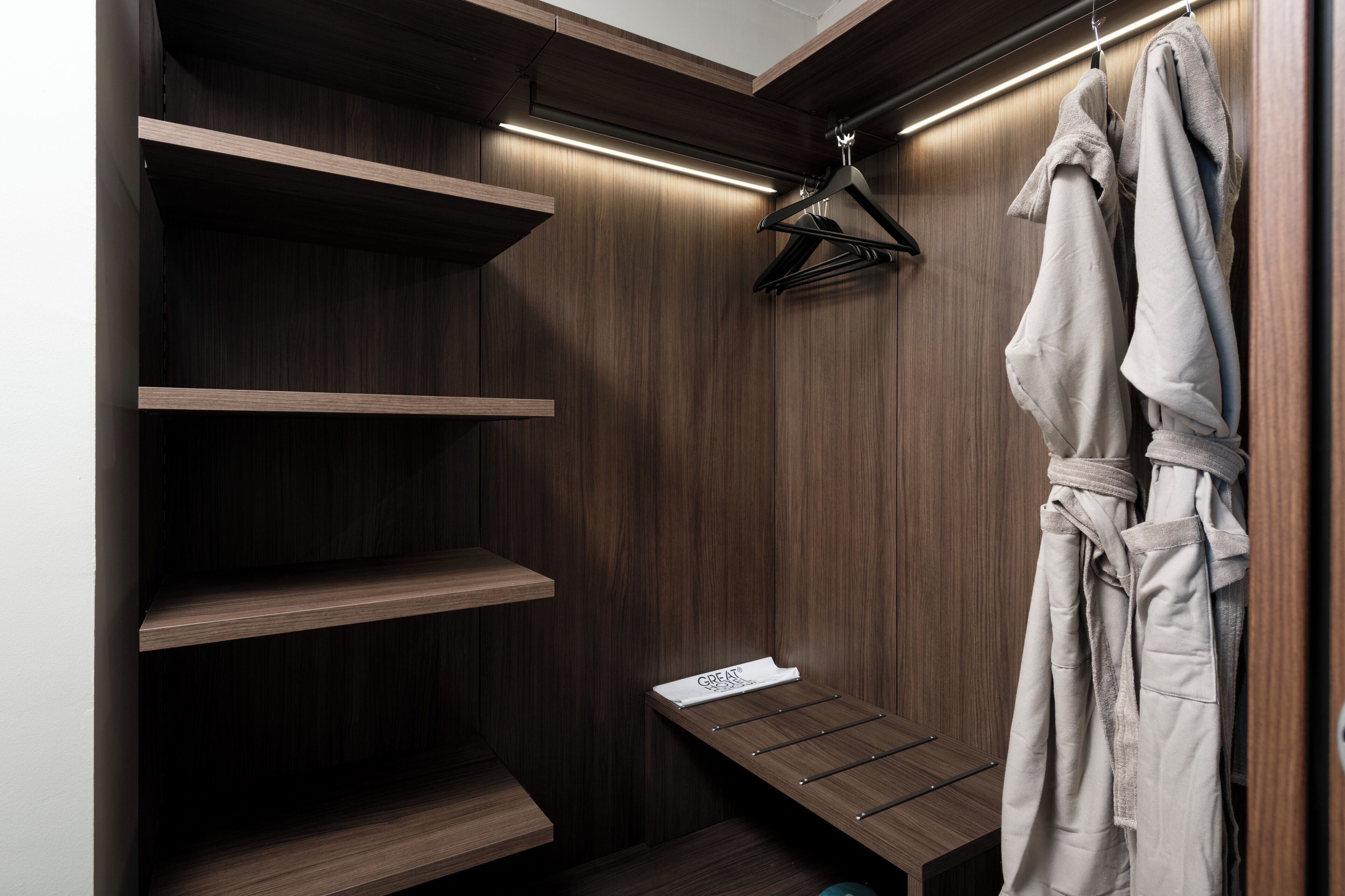 A walk-in closet with wooden shelves, a bench, and a robe hanging on a hanger.