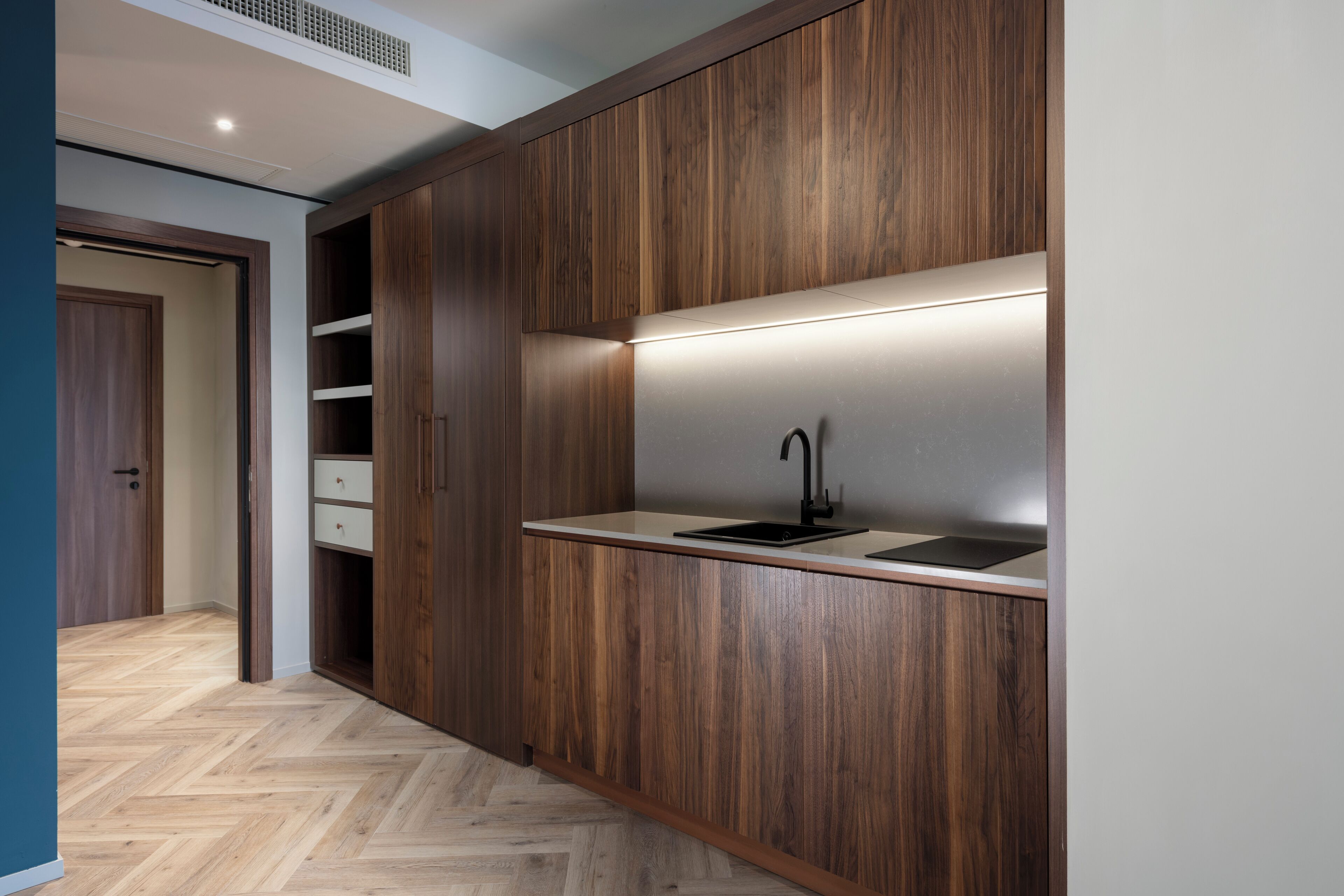 Una cocina moderna con armarios de madera, un lavamanos empotrado y un suelo con patrón de espiga.