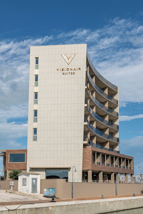 Un edificio alto con diseño moderno, que destaca un logotipo prominente y el nombre 'VISIONAIR SUITES' en la parte superior.
