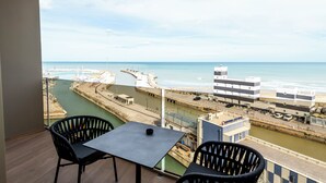 Un balcón con mesa y sillas con vista a un puerto deportivo y una playa.