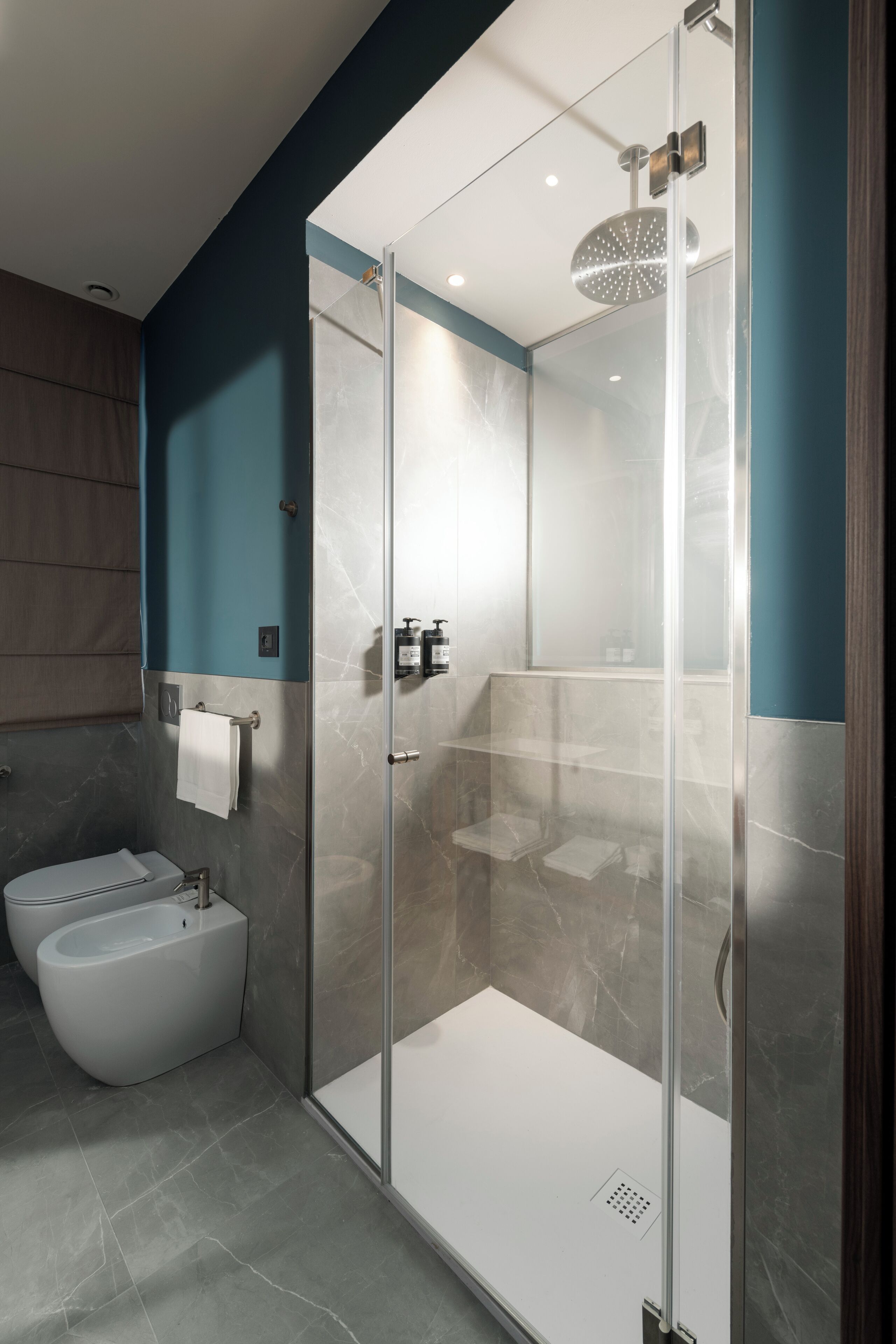 A modern bathroom with a glass-enclosed shower, a standalone bathtub, and marble walls.
