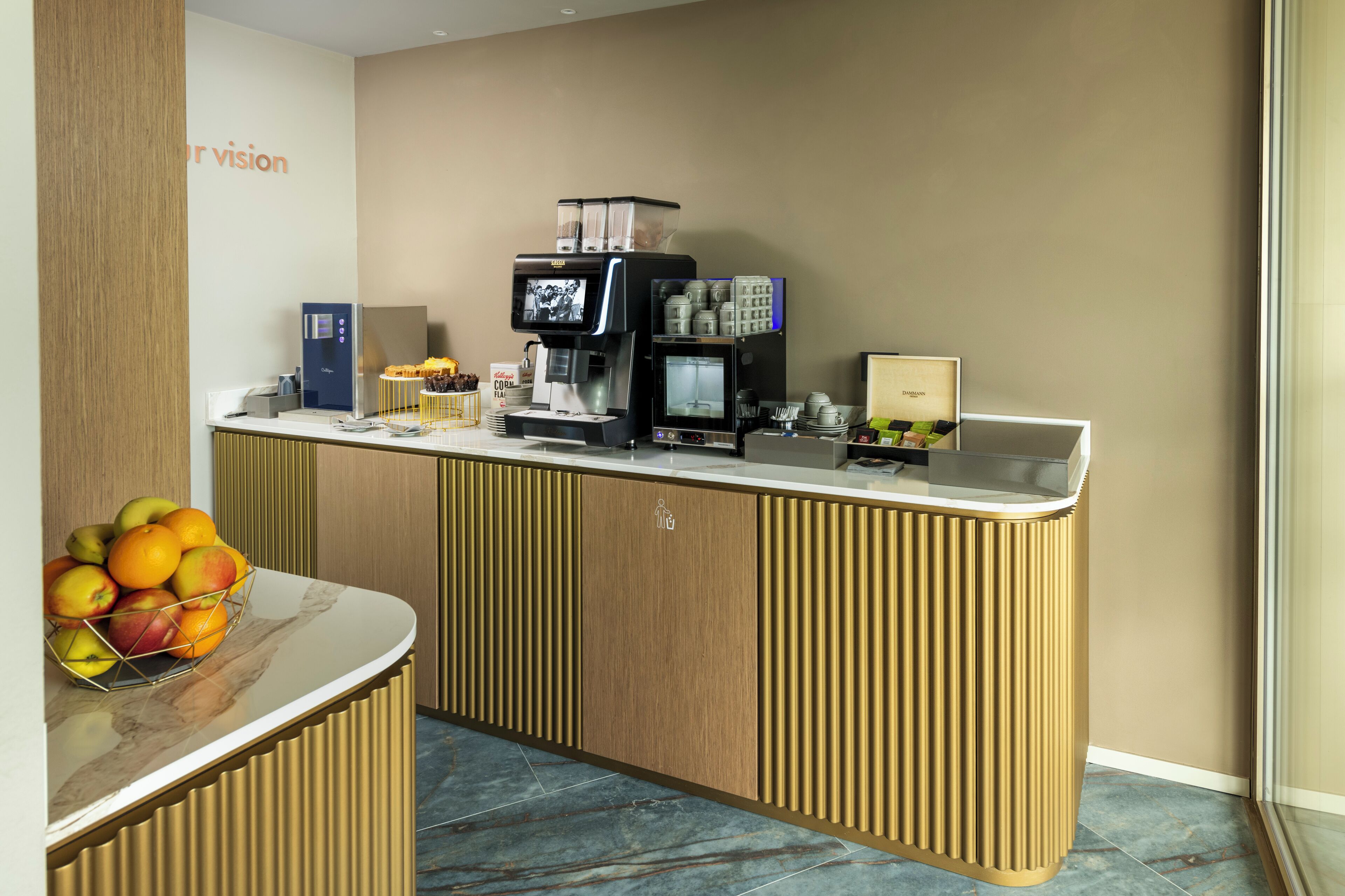 A modern reception area with a coffee machine, a fruit bowl, and a counter with a wooden panel design.