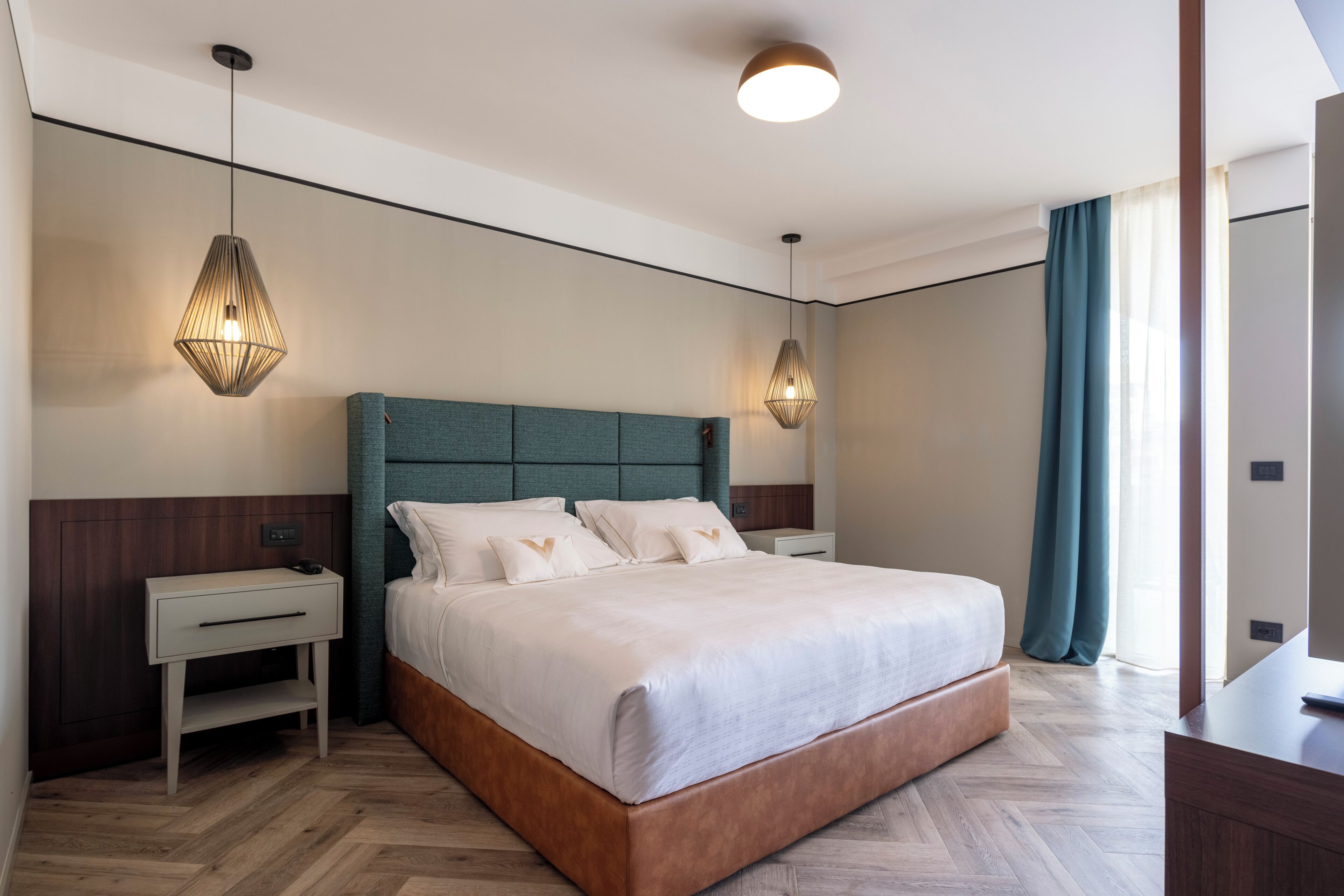 Quarto de hotel moderno com uma cama grande, duas mesas de cabeceira e um criado-mudo.