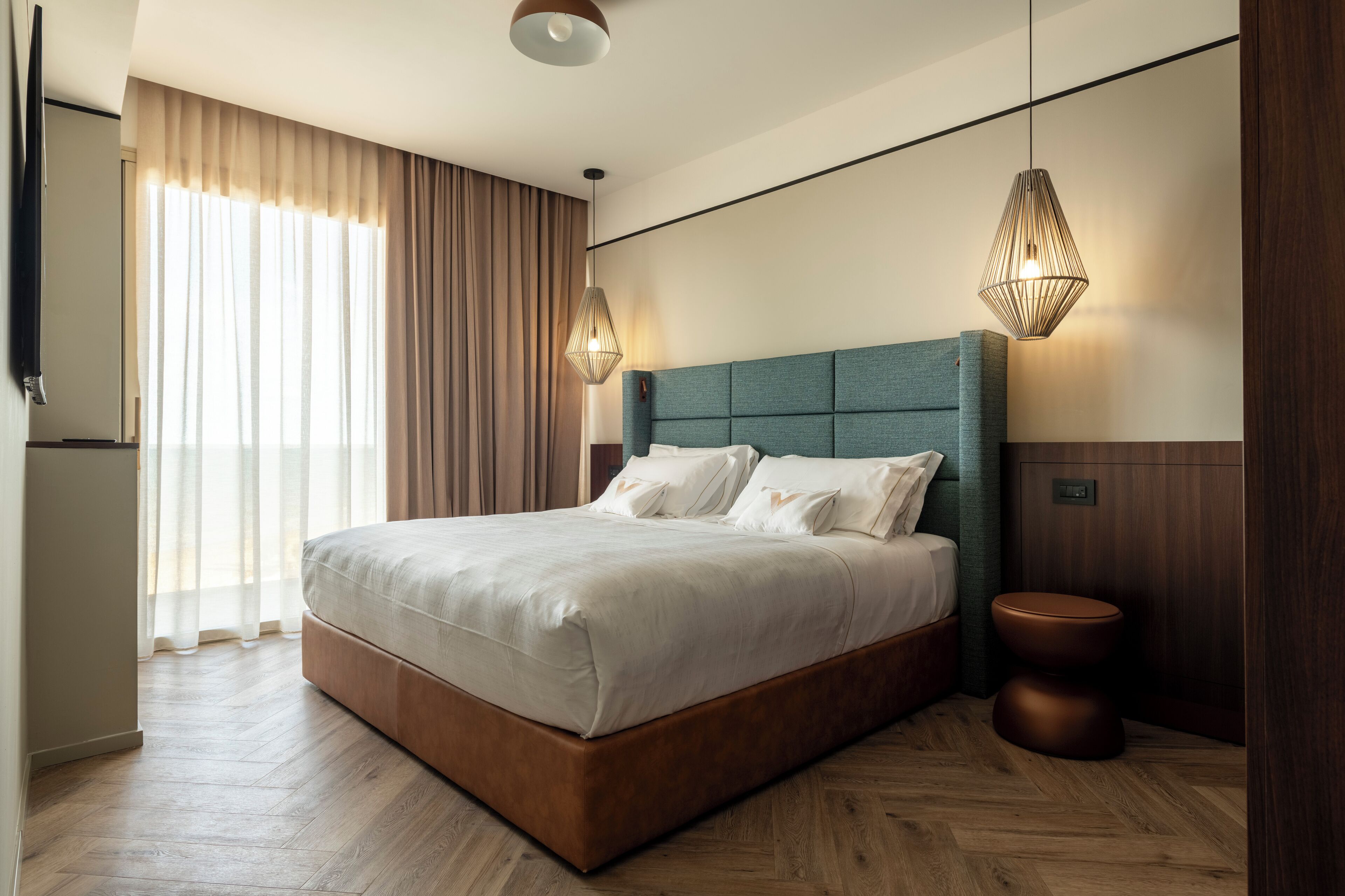 A modern hotel room with a large bed, a wooden floor, a wooden headboard, and two pendant lights.