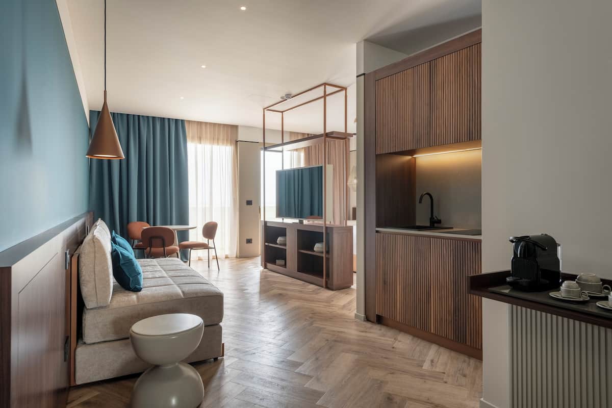 Une chambre d’hôtel moderne équipée d’un canapé, d’une petite table ronde, d’une kitchenette et d’un téléviseur.