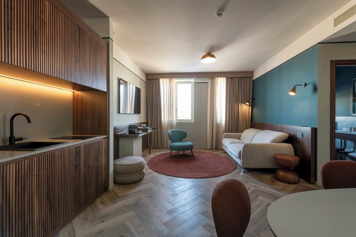 Une chambre d’hôtel moderne équipée d’une kitchenette, d’un canapé, d’un tapis rond et d’un coin repas.