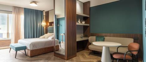 A modern hotel room with a large bed, a sofa, a dining table, and a mirror.