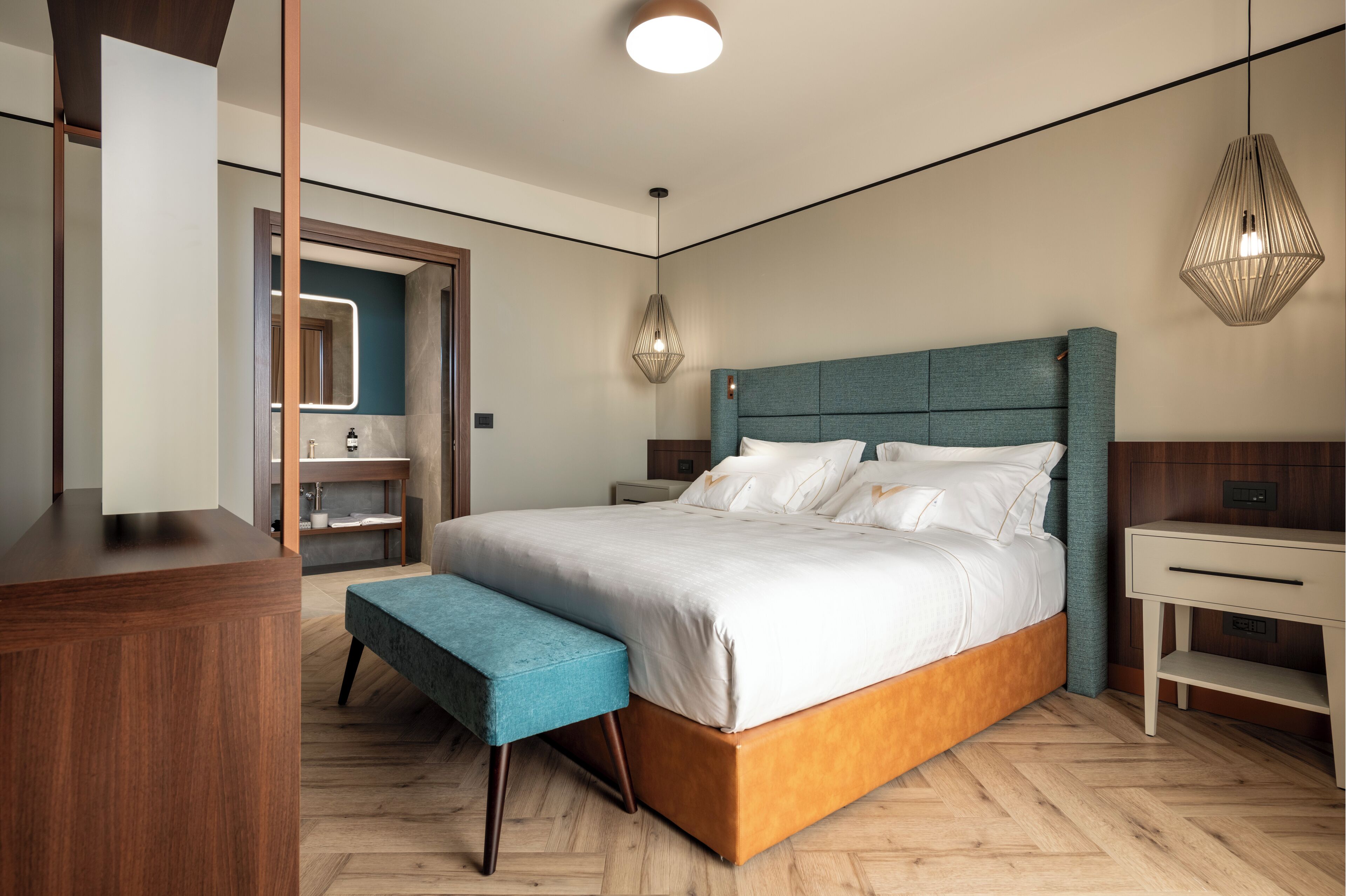 A modern bedroom with a large bed, a wooden bench, a bedside table, and a hanging light fixture.