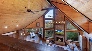 A spacious loft with a high ceiling, wooden beams, a fireplace, and large windows offering views of the outdoors. - Wine Down Ridge- Blue Ridge GA (Blue Ridge)