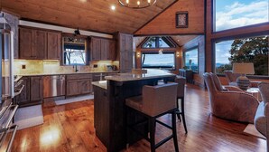 A spacious kitchen with wooden cabinets, a central island, and a large window overlooking a scenic view. - Wine Down Ridge- Blue Ridge GA (Blue Ridge)