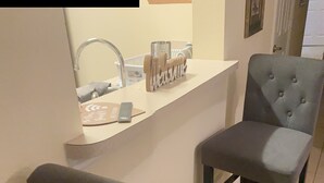 A small kitchen area with a white countertop, a sink, and a chair.