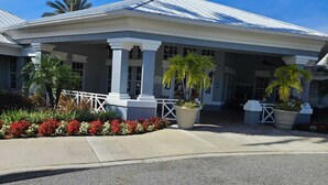 A building with a covered entrance, white columns, and a small tower. There are potted plants and flowers in front.