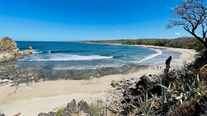 Eine Küstenlandschaft mit Sandstrand, klarem, blauem Meer und Felsformationen.