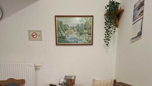 Ein kleiner Raum mit einem Holztisch, zwei Stühlen, einer Couch, einem Heizkörper, einem gerahmten Gemälde und einer Pflanze.