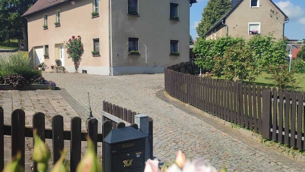 Ein zweistöckiges Haus mit geneigtem Dach, einer gepflasterten Auffahrt und einem Holzzaun.