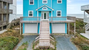 A two-story house with a front porch, a garage, and a wooden staircase leading to the entrance. - Renegade | Oceanfront + Room for the Whole Family! (Surf City)
