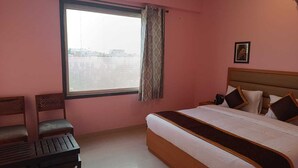 A bedroom with a bed, a window with blinds, a chair, and a picture on the wall. - The Kapji Palace (Jaipur)
