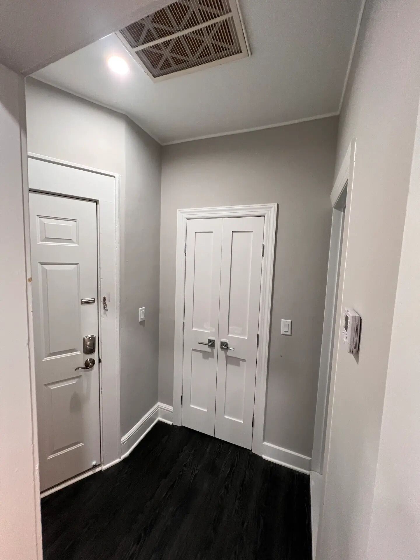 Un couloir avec deux portes blanches, un plancher noir et une bouche d’aération au plafond.