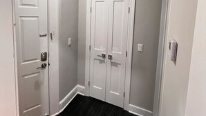 Un couloir avec deux portes blanches, un plancher noir et une bouche d’aération au plafond.