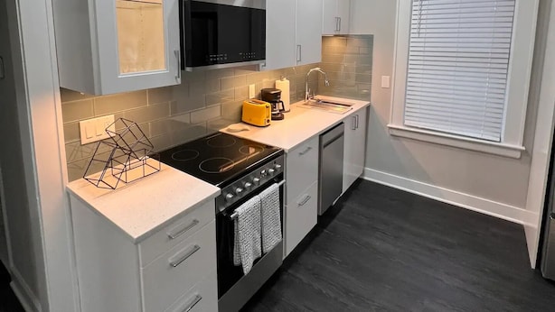 Une cuisine moderne avec des meubles blancs, un micro-ondes noir, une cuisinière et un évier.