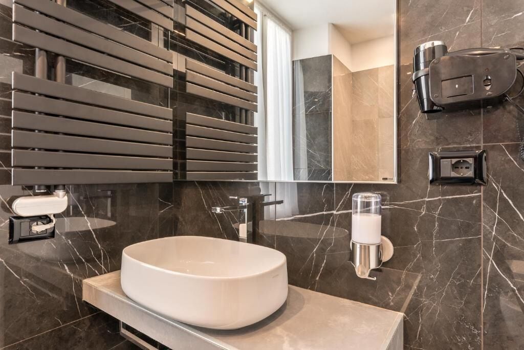 Une salle de bain moderne avec un grand lavabo ovale, un miroir, un distributeur de serviettes et un sèche-cheveux fixé au mur.