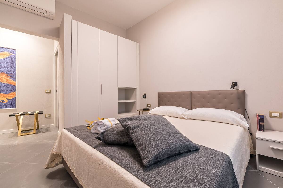 Een slaapkamer met een bed, nachtkastjes, een kledingkast en een schilderij aan de muur.