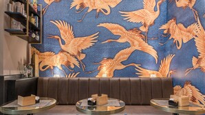 Een restaurantinterieur met een patroonmuur, lederen zitplaatsen en ronde tafels.