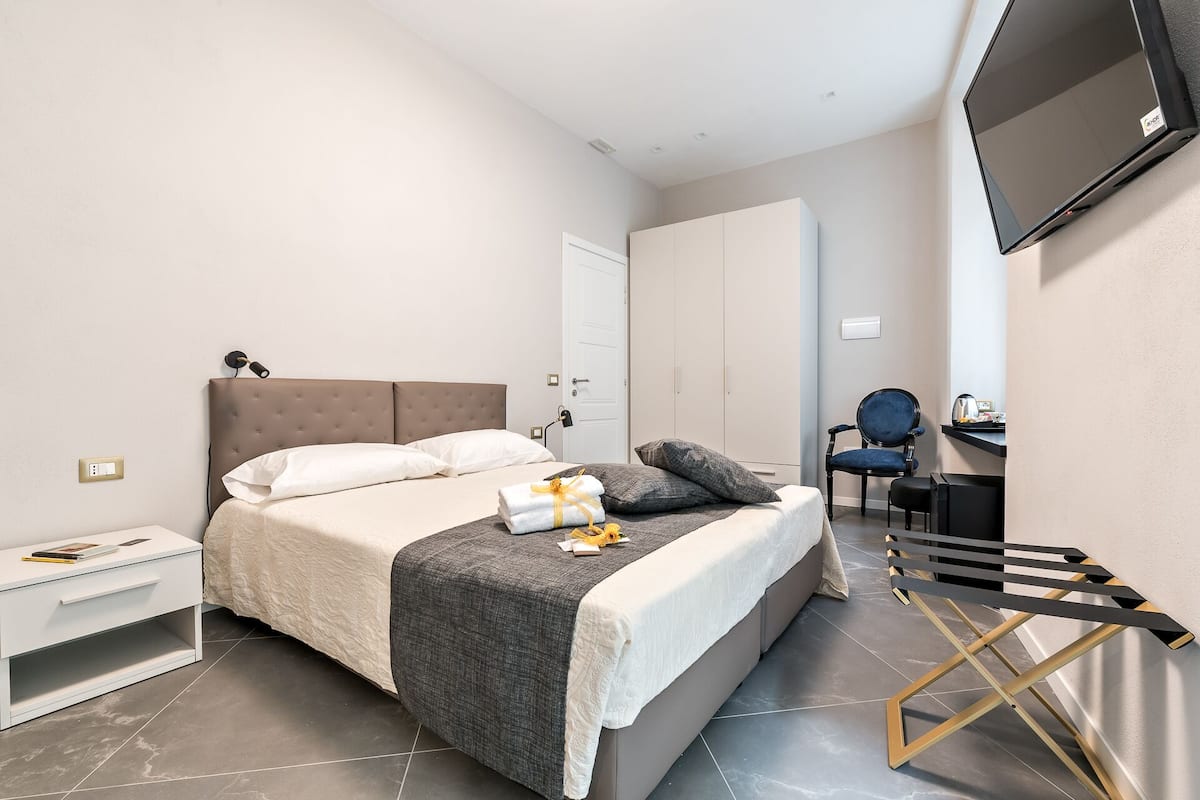 Een moderne slaapkamer met een bed, nachtkastje, stoel, bureau en een aan de muur bevestigde televisie.