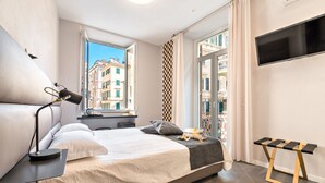 Een moderne slaapkamer met een groot bed, een nachtkastje, een lamp, een televisie en een raam met uitzicht op de stad.