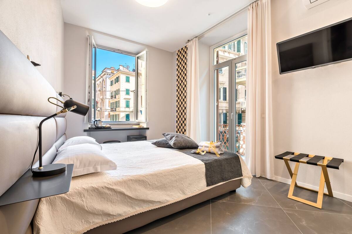 Een moderne slaapkamer met een groot bed, een nachtkastje, een lamp, een televisie en een raam met uitzicht op de stad.